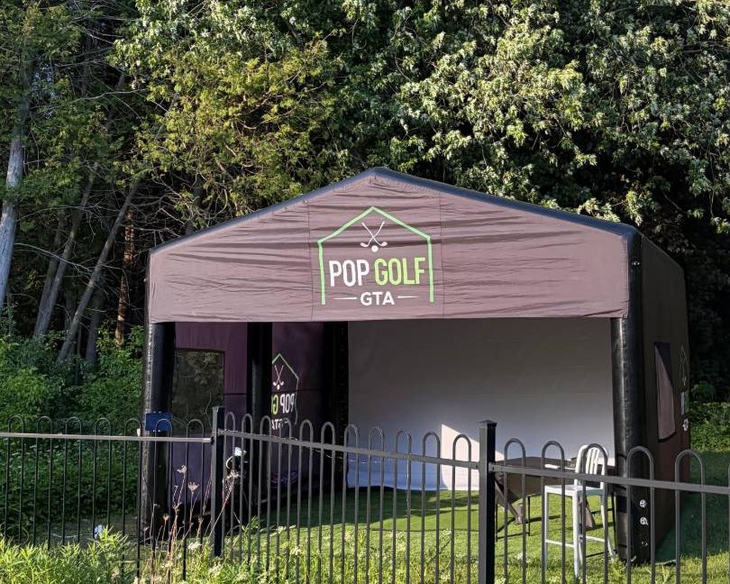 Pop Golf GTA branded golf simulator enclosure set up outdoors on a lawn surrounded by trees
